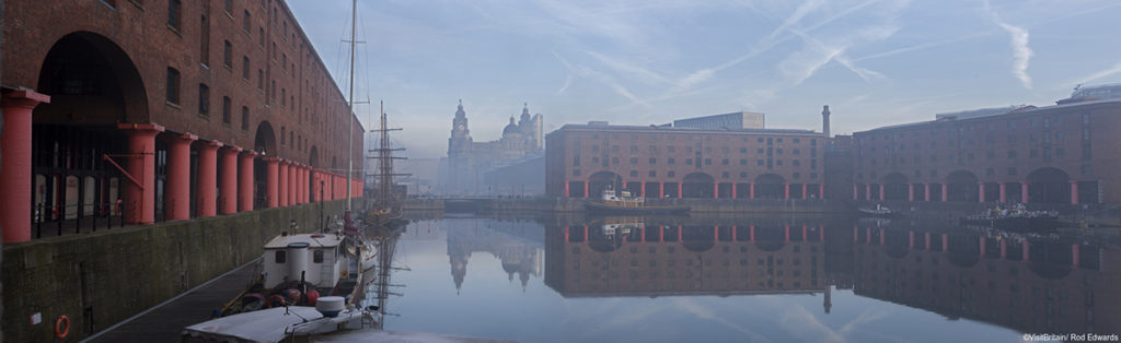 Maritime Albert Dock on Liverpool waterfront with the Three Graces historic buildings. The Liverpool world heritage site. Port of Liverpool building, the Cunard Building and the Liver building. A historic ship moored. Mist rising from the water.