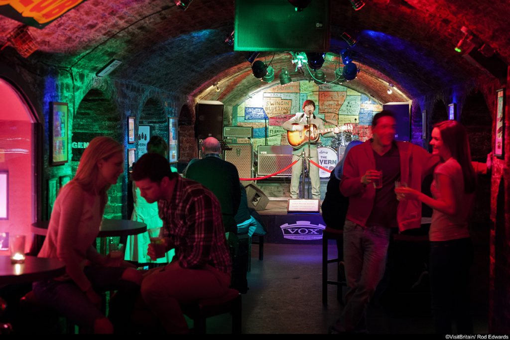 The Cavern Club in Liverpool, the club in Matthew Street where the Beatles music group started their career. The club in a cellar with low arched ceilings. People sitting at tables. Coloured lights and view to the stage. ©Visit Britain/Rod Edwards
