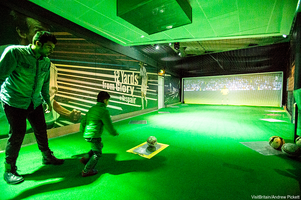 The National Football Museum. Photo: VisitBritain/Andrew Pickett A father and son visiting the museum. Kicking a football and aiming at a goal. 