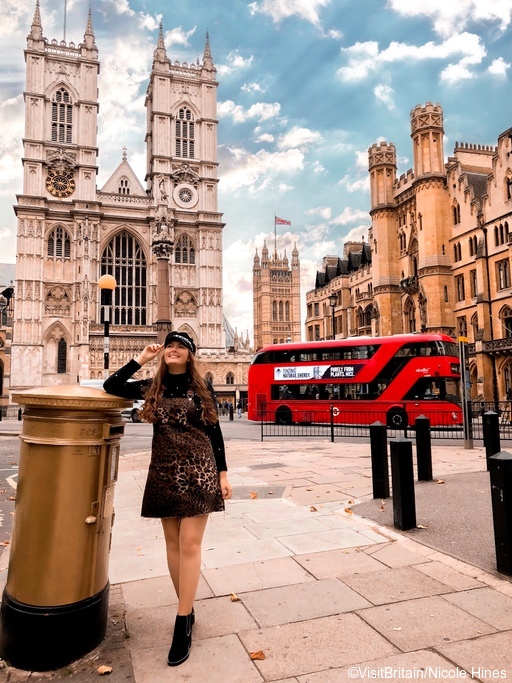 A girl standing by a golden letter box in front of Westminster Abbey with a red bus behind. ©VisitBritain/Nicole Hines