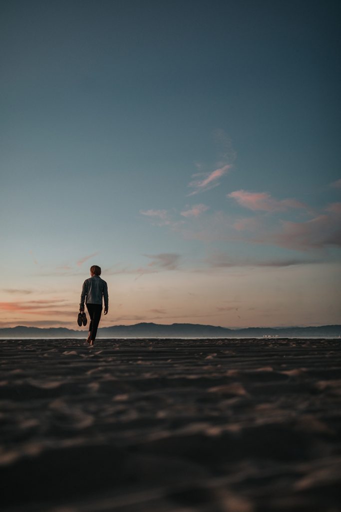 Man walking on beach. Photo by Nathan Dumlao on Unsplash