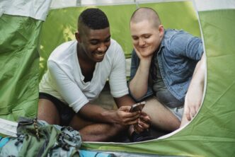 Laughing man showing phone to friend in tent