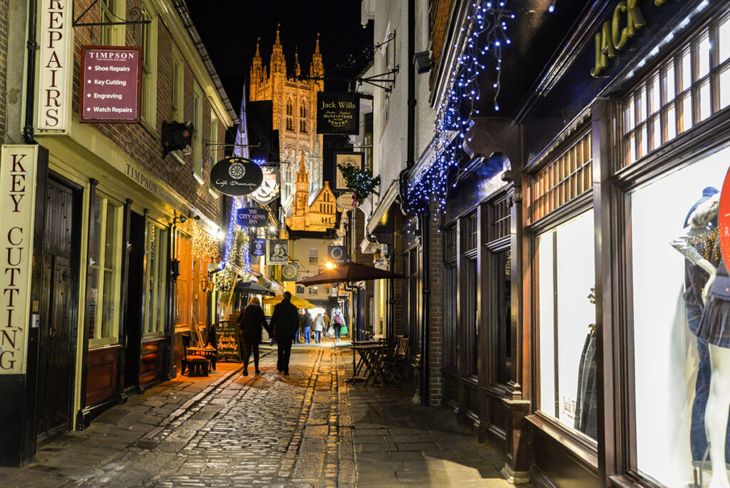 People walking along street at night, Canterbury, Kent, England.